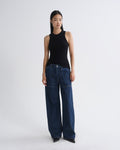 A model stands against a light gray studio background wearing a black sleeveless ribbed top and dark blue wide-leg denim jeans.