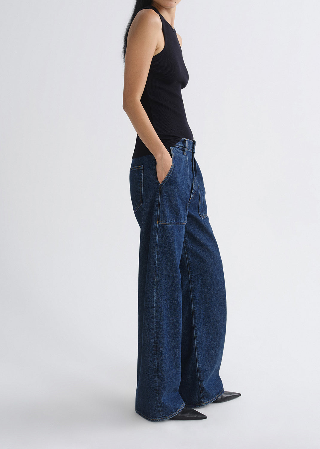 Person wearing blue wide-leg jeans and a black top on a grey background