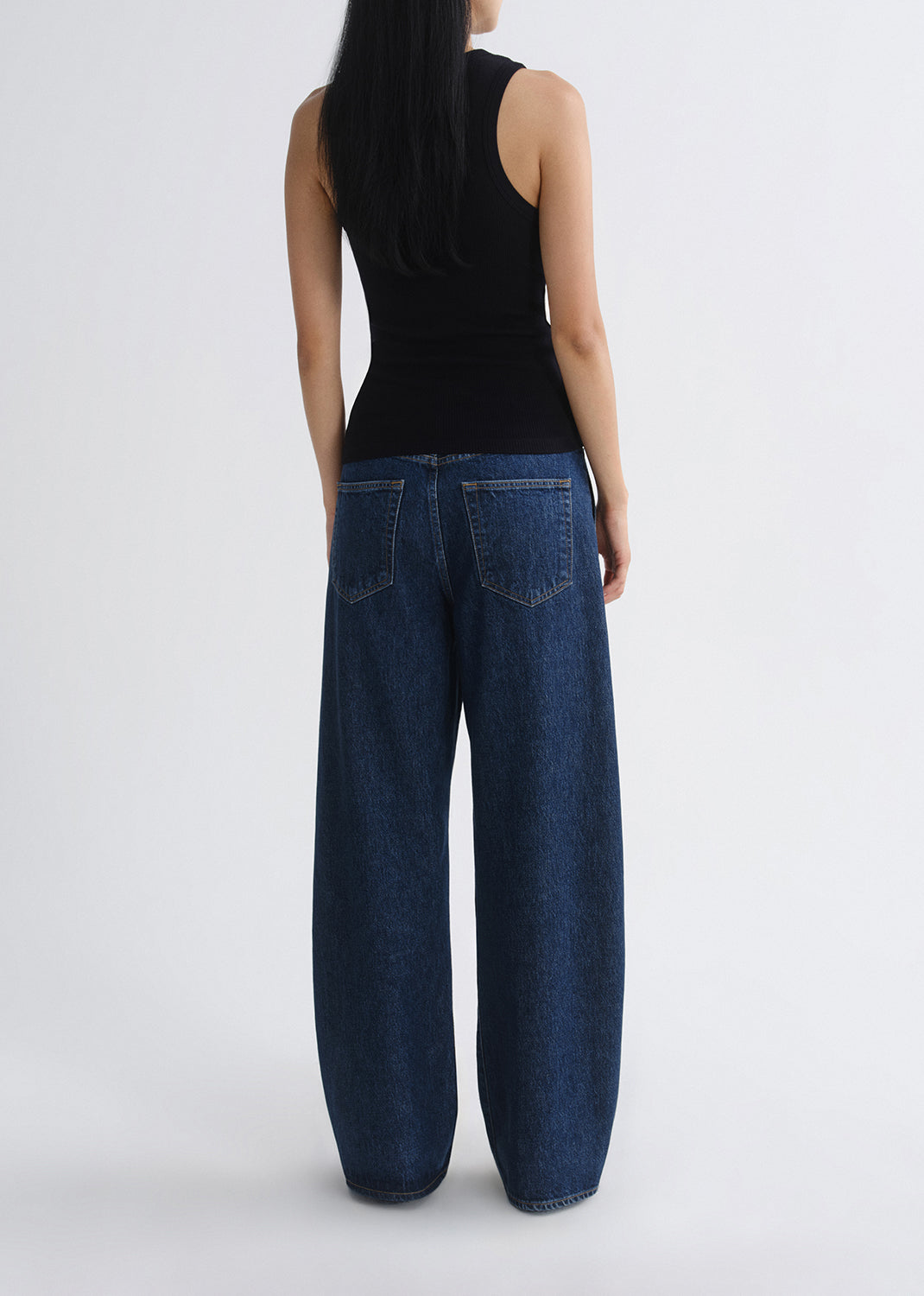 Person wearing blue jeans and a black top on a grey background