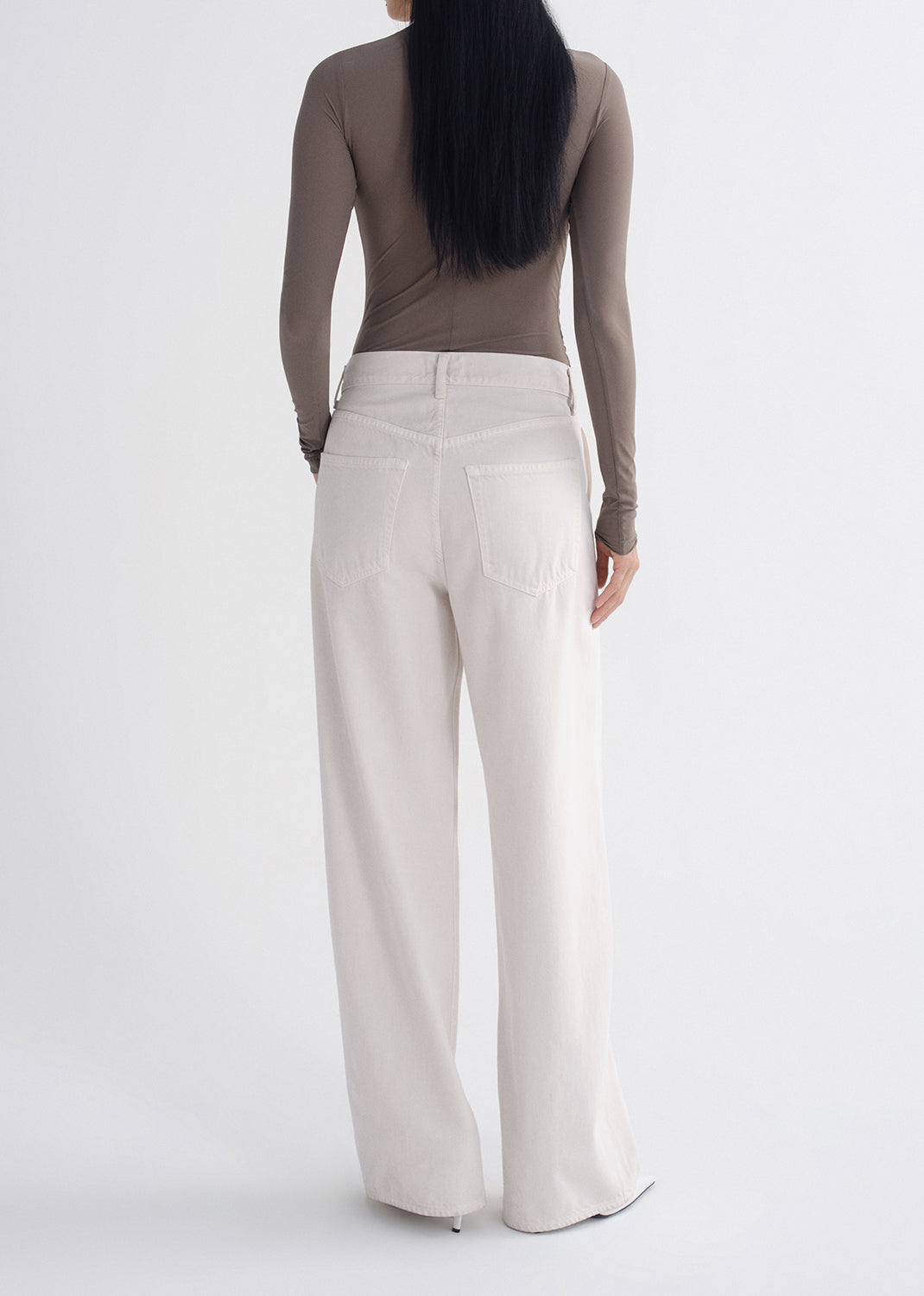 Person wearing a brown long-sleeve top and white wide-leg pants on a grey background