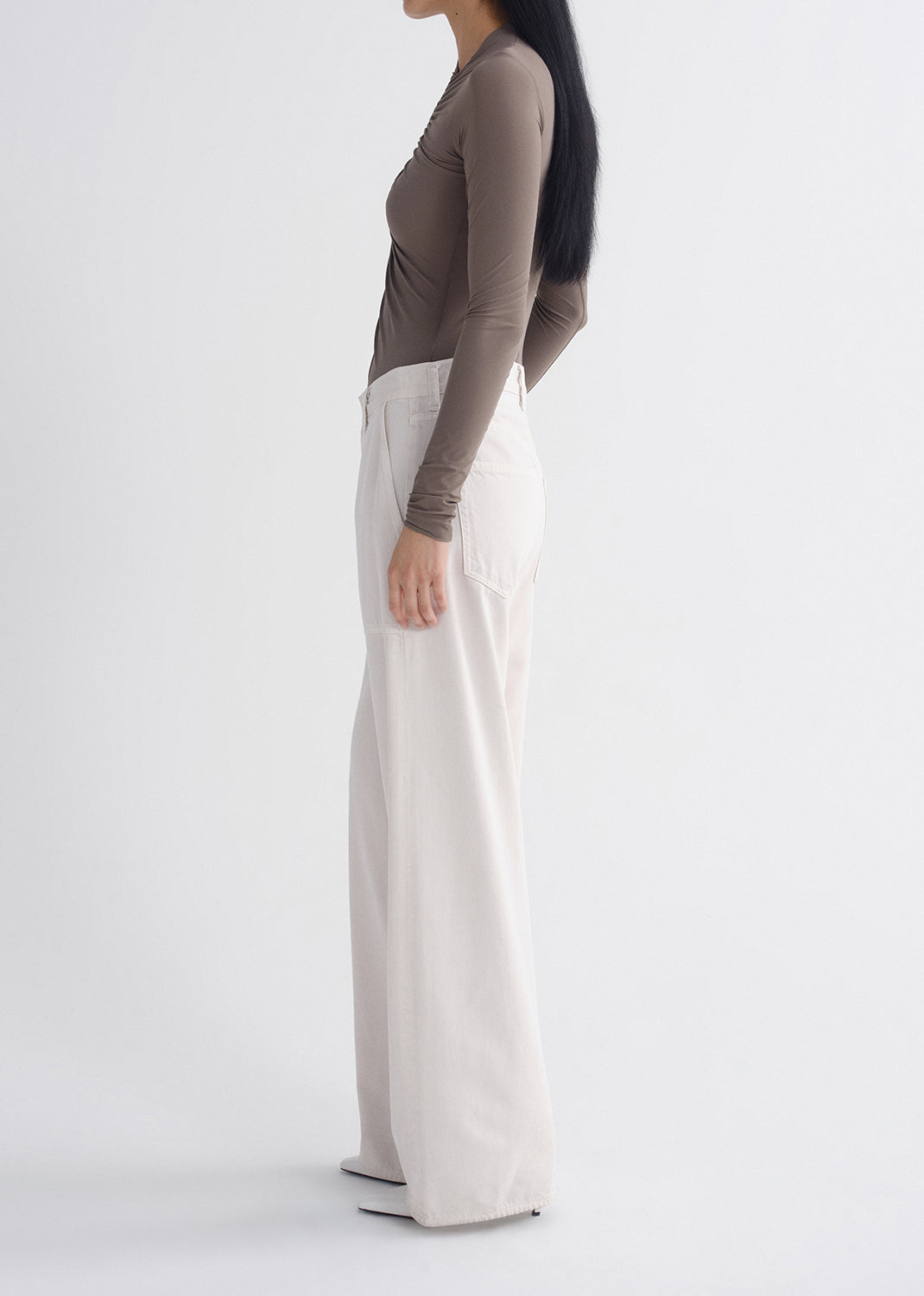 Person wearing a brown top and white pants on a grey background