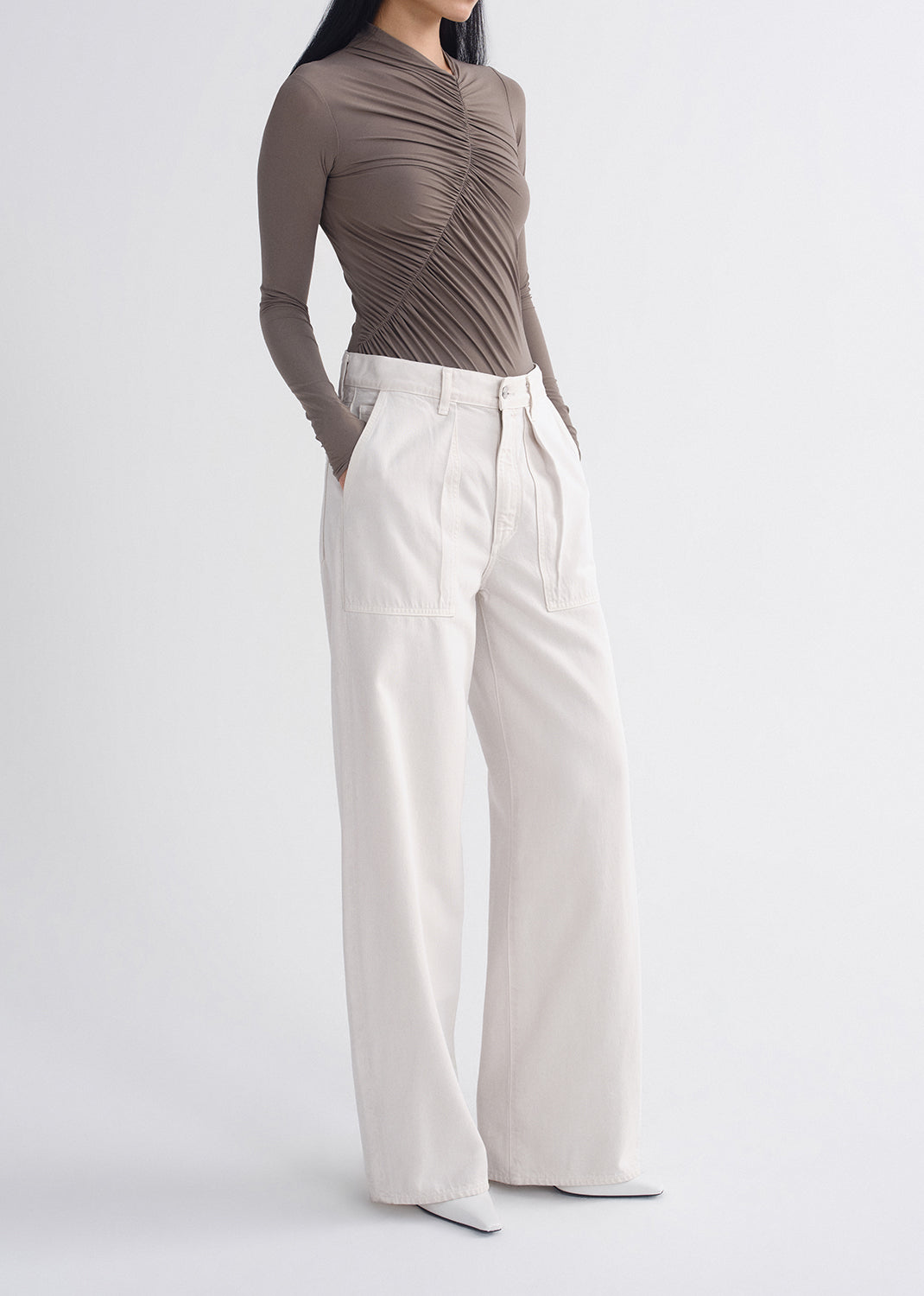 Person wearing a brown ruched top and white pants on a grey background
