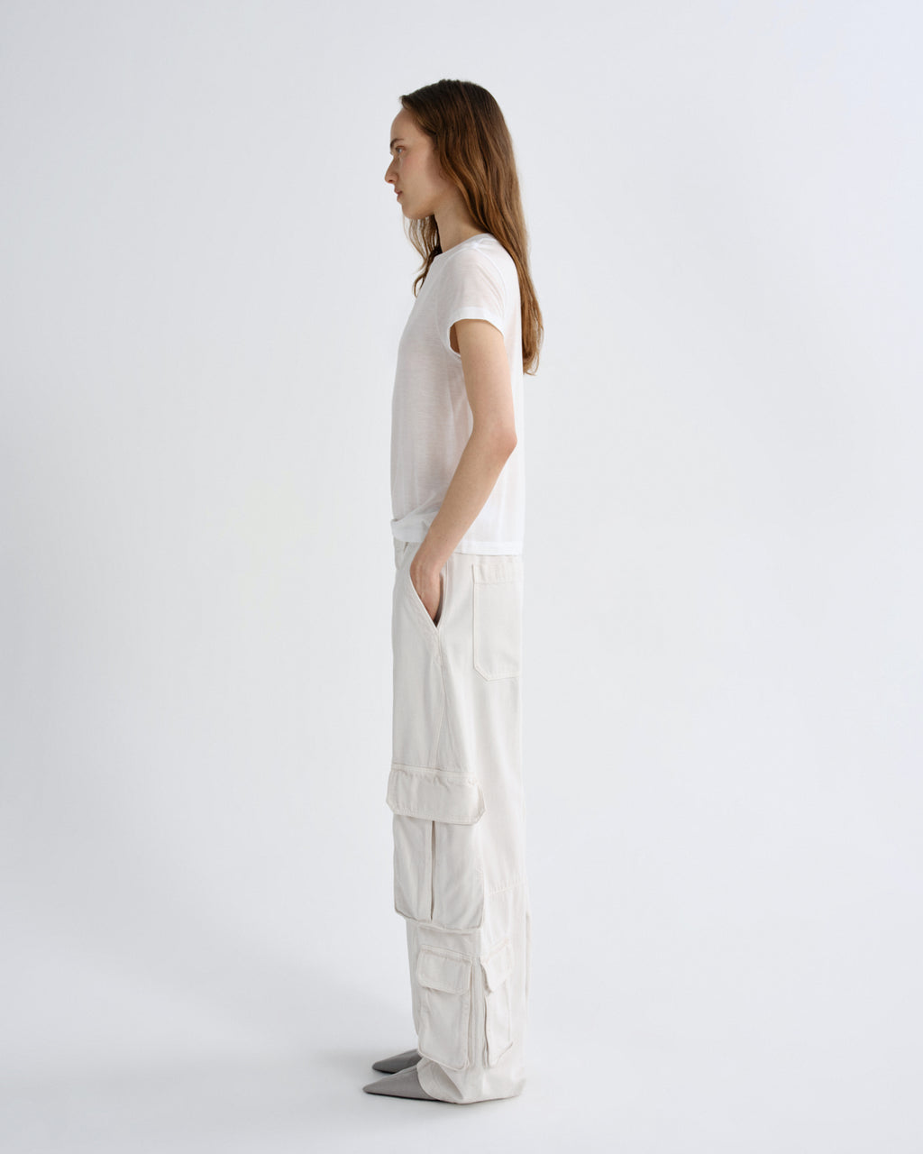 A model stands in profile wearing a white short-sleeve top and off-white wide-leg cargo pants against a plain light gray studio background.