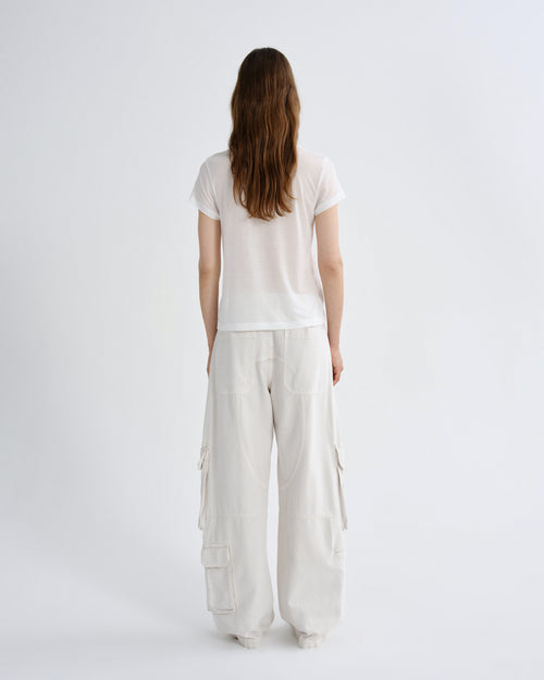 A woman viewed from behind wearing a white short-sleeve t-shirt and off-white wide-leg cargo pants against a plain white studio background.