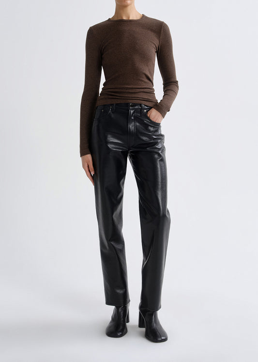 Person wearing a brown fitted long sleeve top with black straight leg leather pants on a grey background