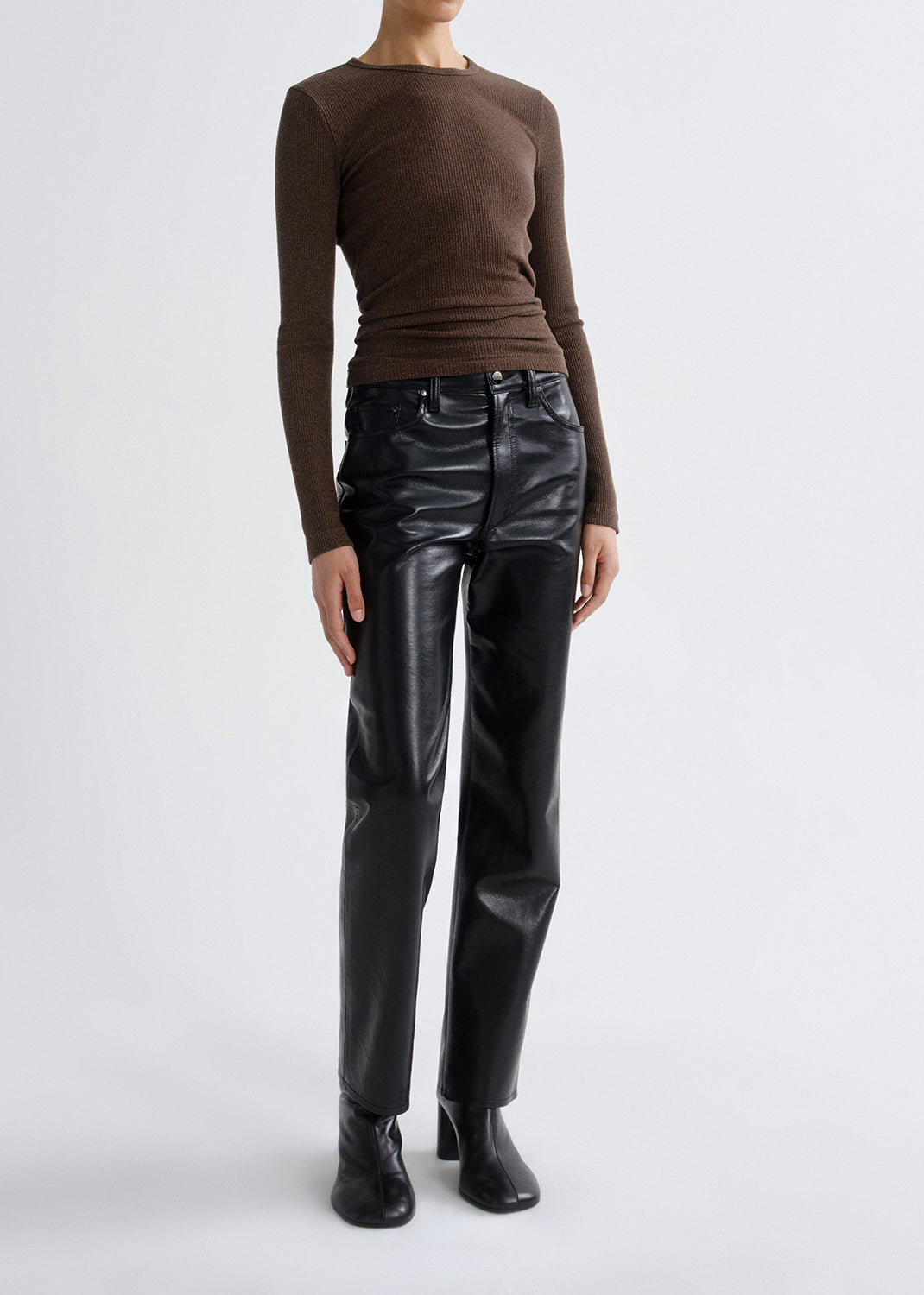 Person wearing a brown fitted long sleeve top with black straight leg leather pants on a grey background