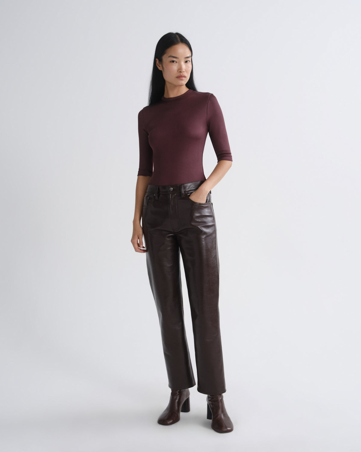 Woman wearing a burgundy top and brown leather pants on a white background