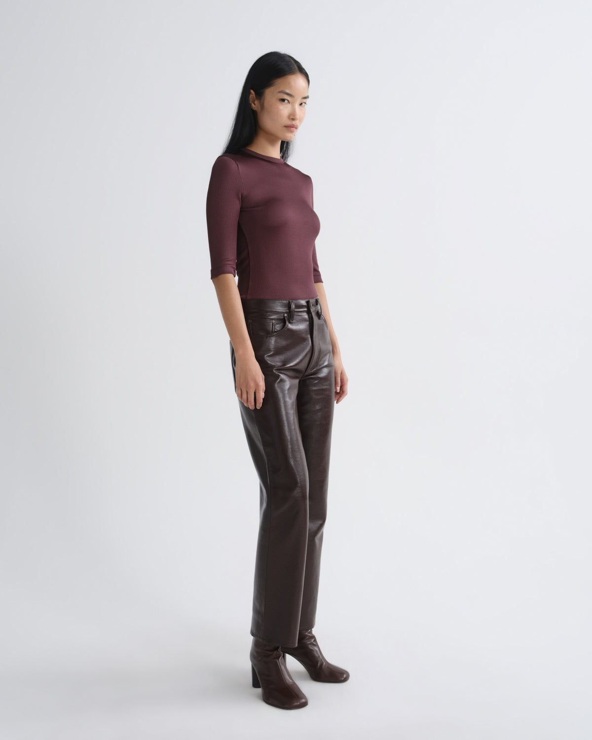 Woman wearing a maroon top and brown leather pants on a white background