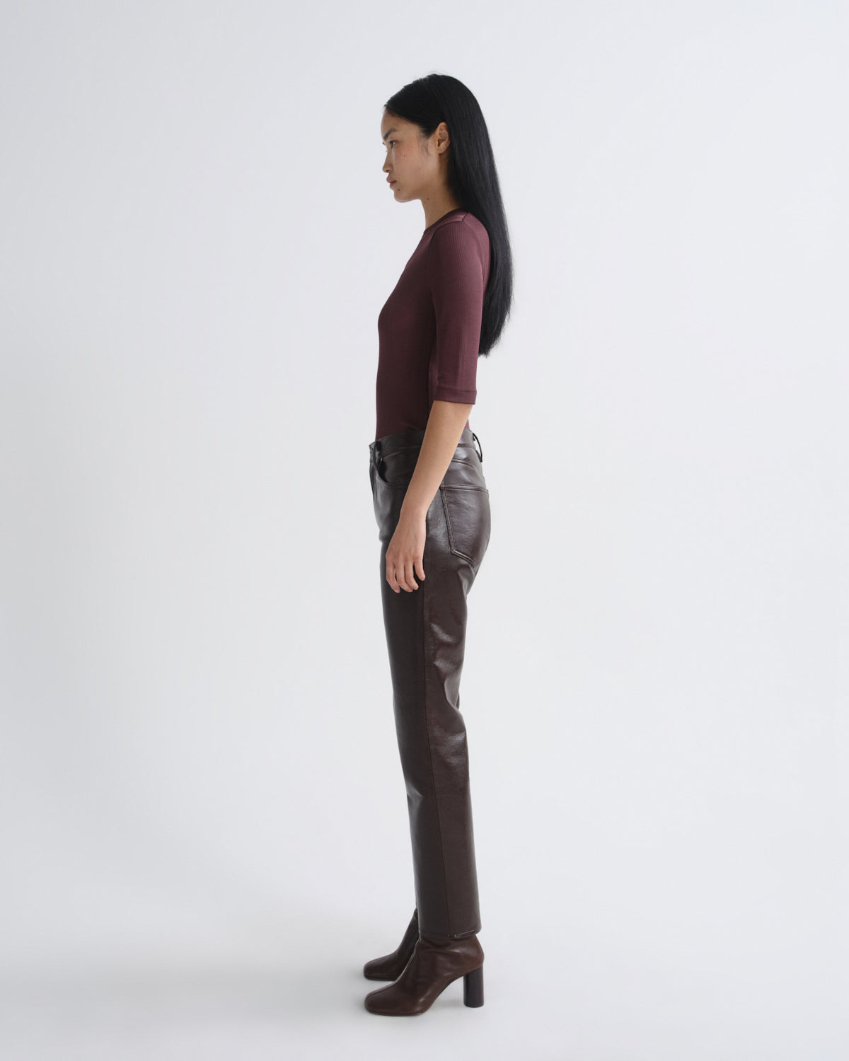 Woman wearing a burgundy top and brown leather pants on a white background