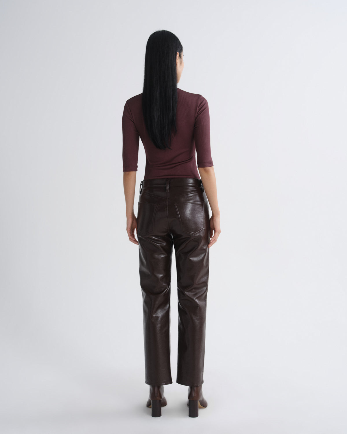 Person wearing a burgundy top and brown leather pants on a white background