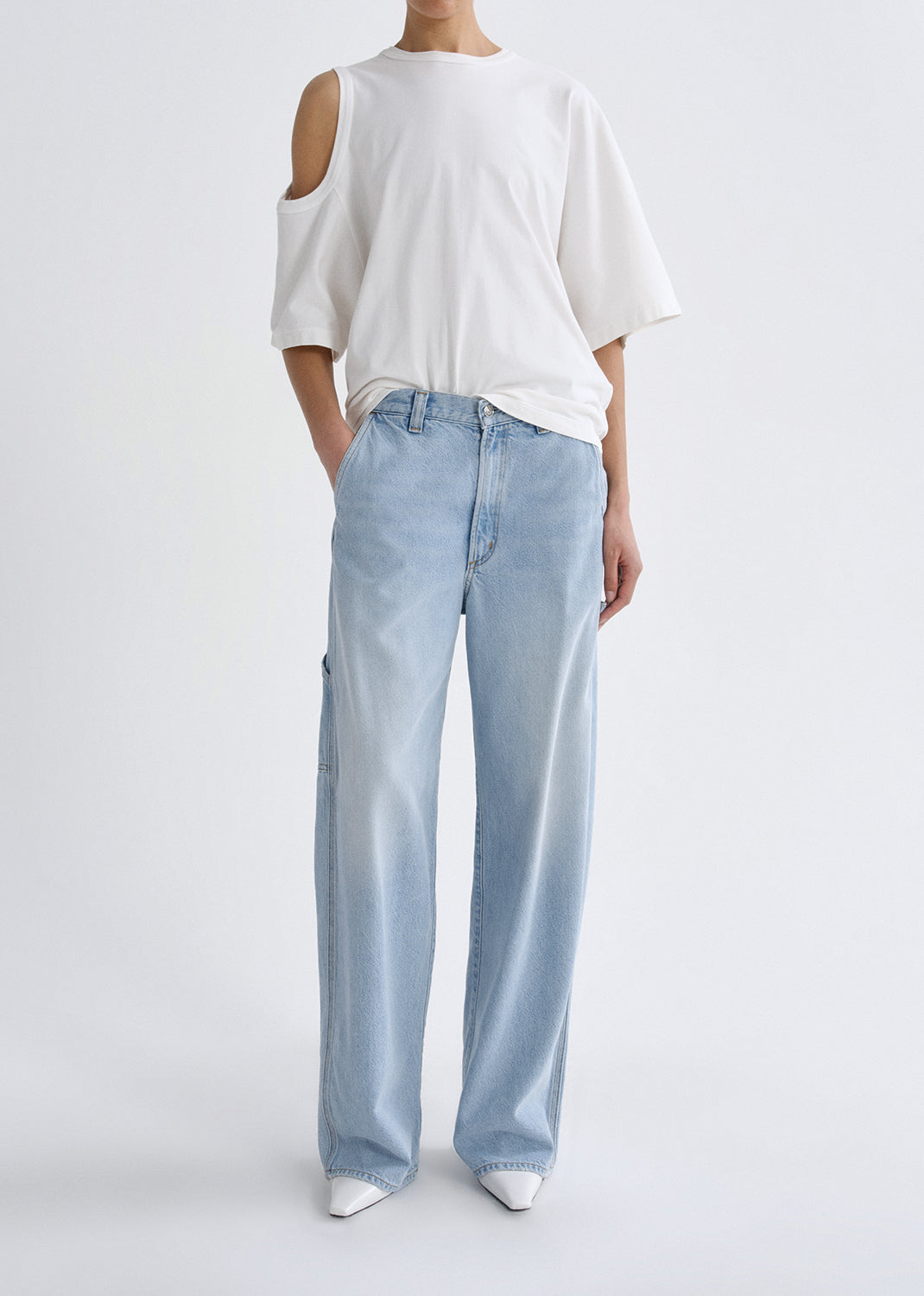 Person wearing a white oversized shirt and light blue jeans on a grey background