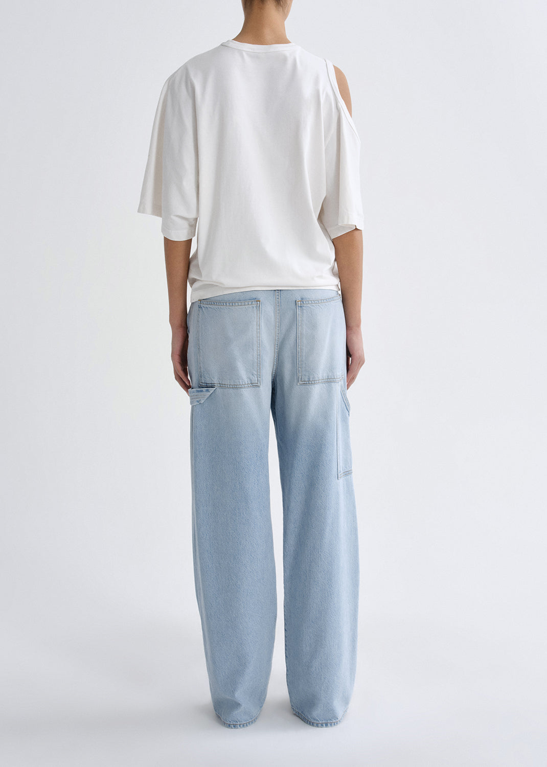 Person wearing a white t-shirt and light blue jeans on a grey background