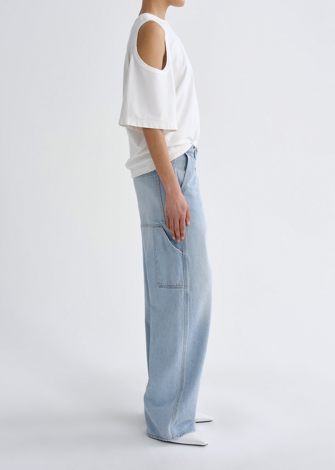 Person wearing a white off-shoulder top and light blue jeans on a grey background