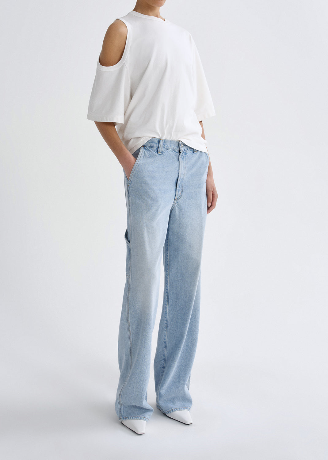 Person wearing a white off-shoulder top and light blue jeans on a grey background