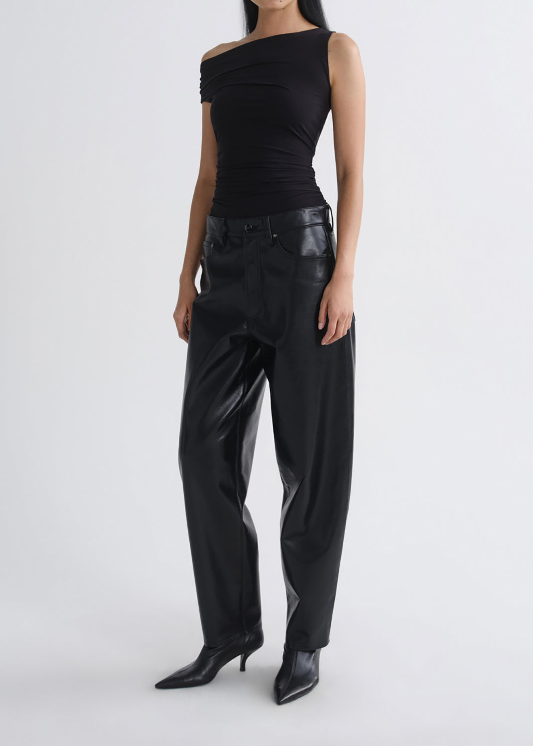 A model wearing a black off-the-shoulder sleeveless top and black wide-leg pants with a glossy finish, paired with black pointed-toe heeled boots, against a grey background.