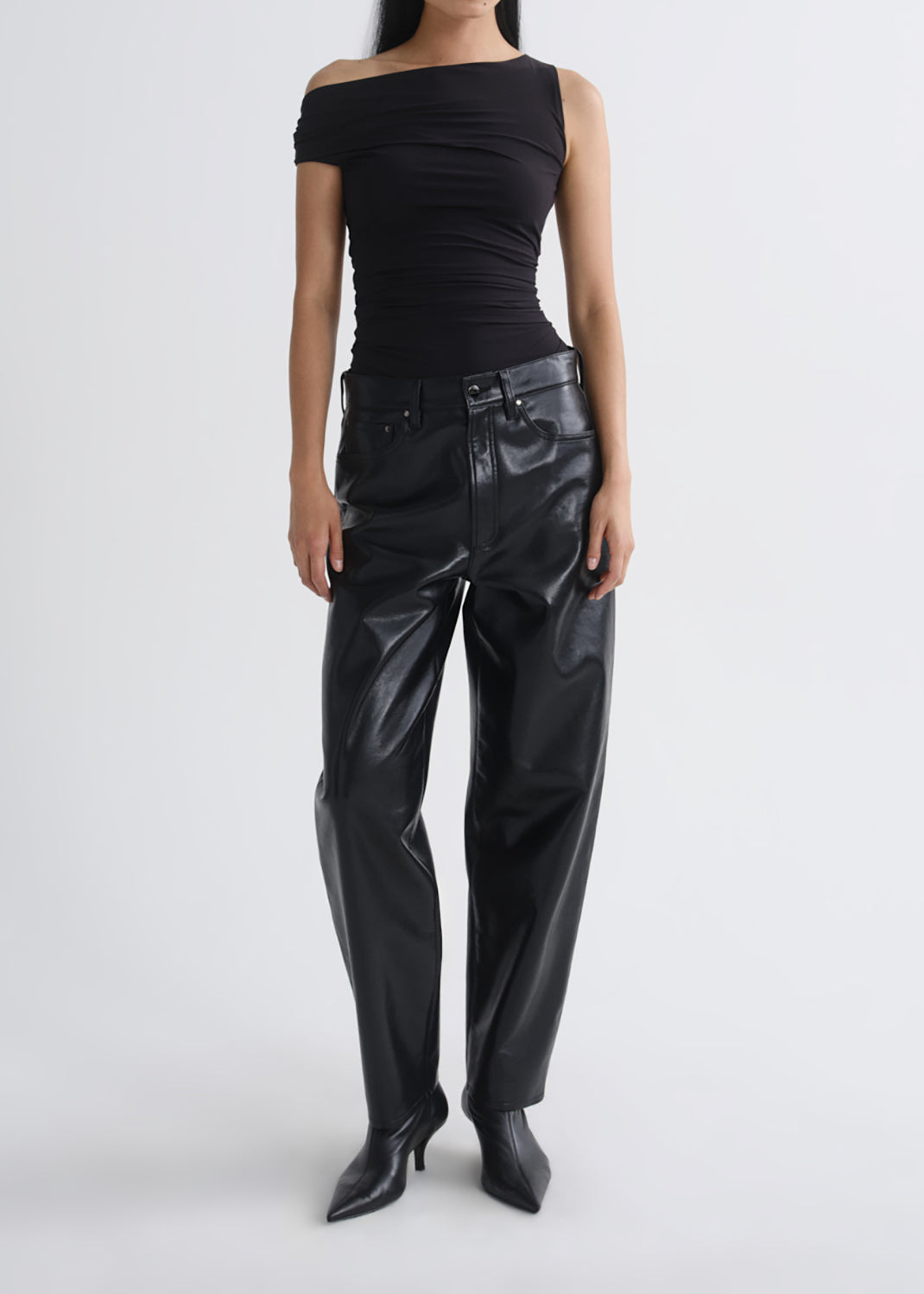 A model wearing a black off-the-shoulder ribbed top, black faux-leather wide-leg pants, and black pointed-toe heeled boots, photographed against a grey background.