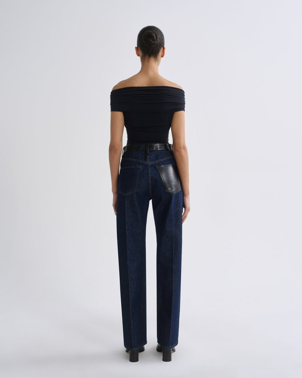 Woman wearing dark indigo straight leg jeans with a black off-the-shoulder top viewed from the back on a grey background.