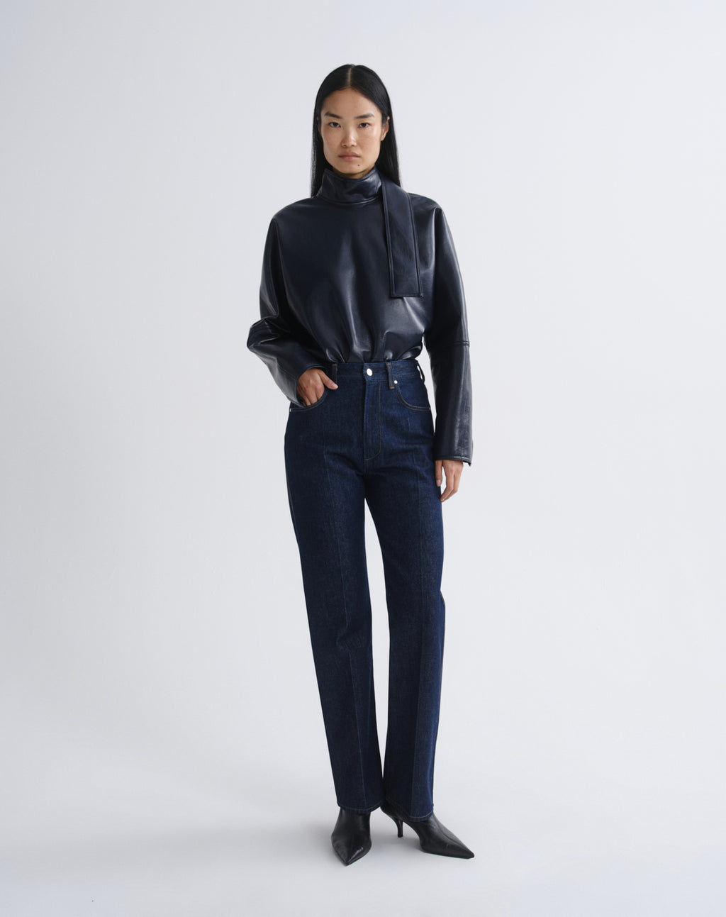 Person wearing a navy satin button-up shirt with dark indigo straight leg jeans on a grey background