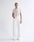 A model stands against a plain white studio background wearing a loose white short-sleeve top and matching white wide-leg trousers with rolled cuffs.
