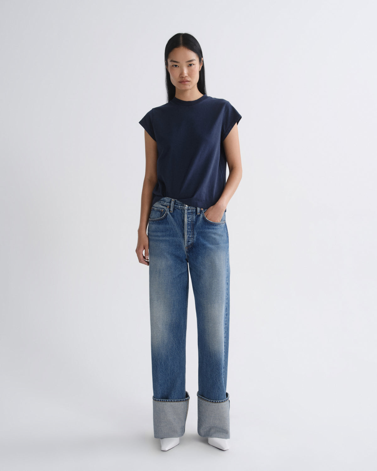 Person wearing a navy top and blue jeans on a white background