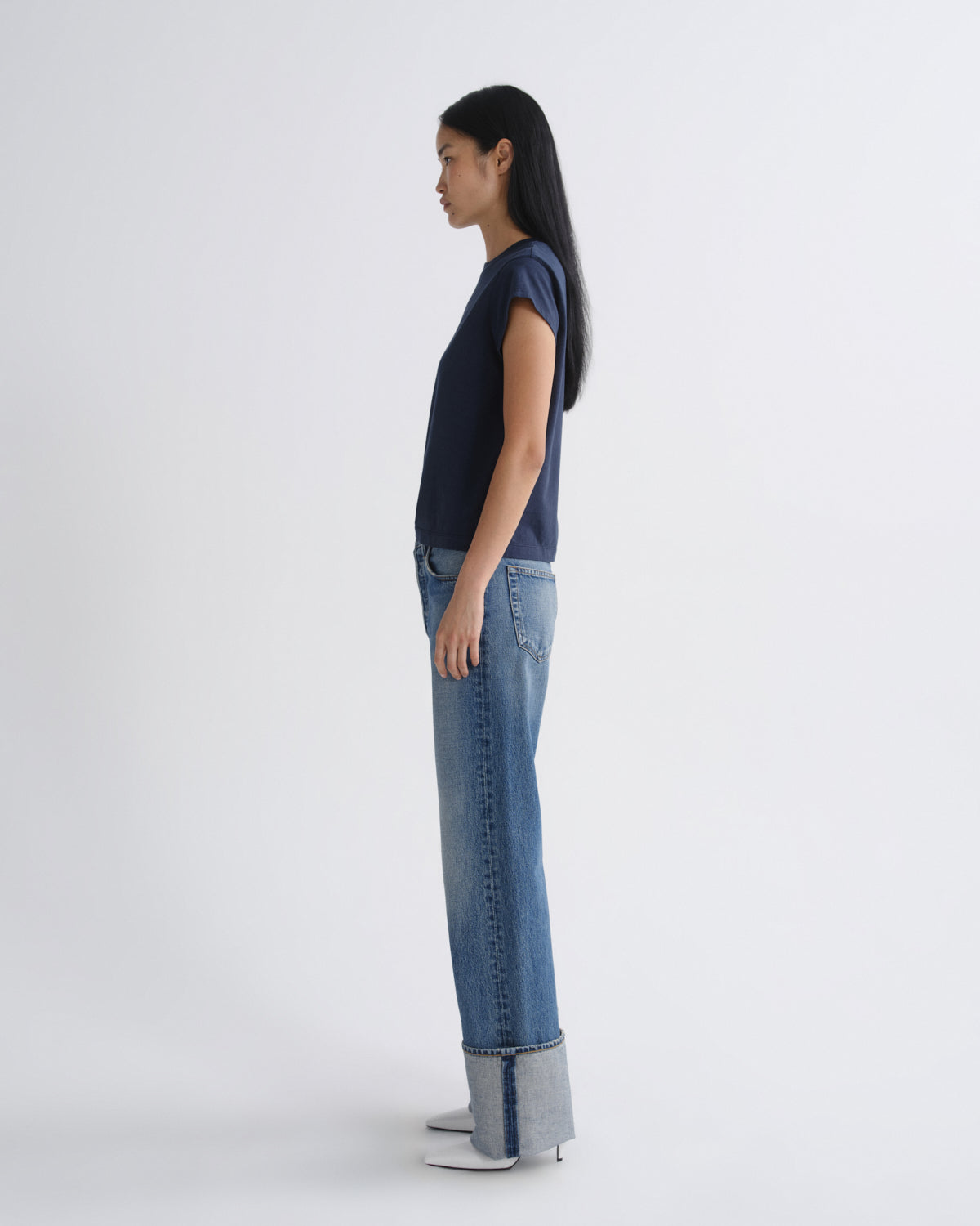 Woman wearing a navy top and blue jeans with a white background