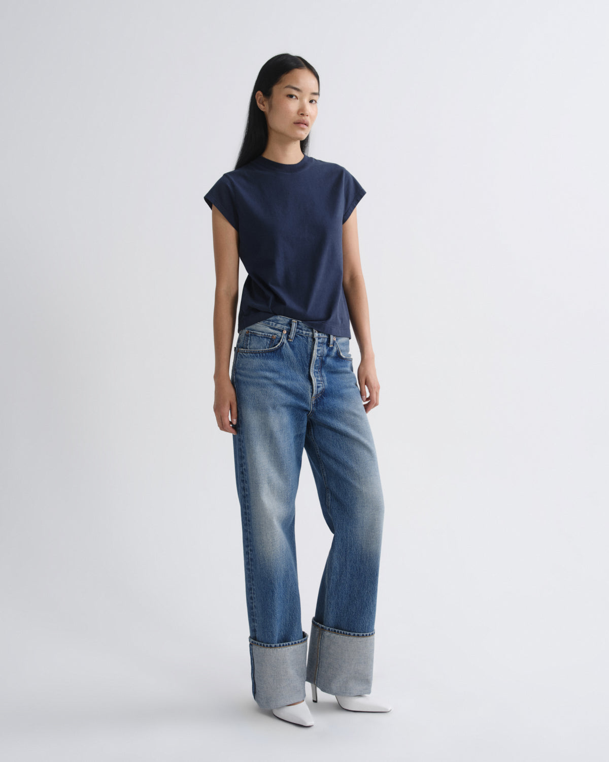Woman wearing a navy top and blue jeans on a white background