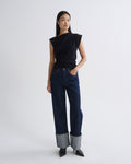 Woman wearing a navy sleeveless top and dark blue jeans on a white background