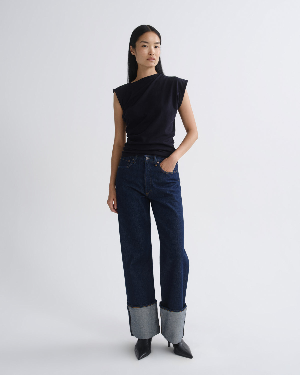 Woman wearing a navy sleeveless top and dark blue jeans on a white background