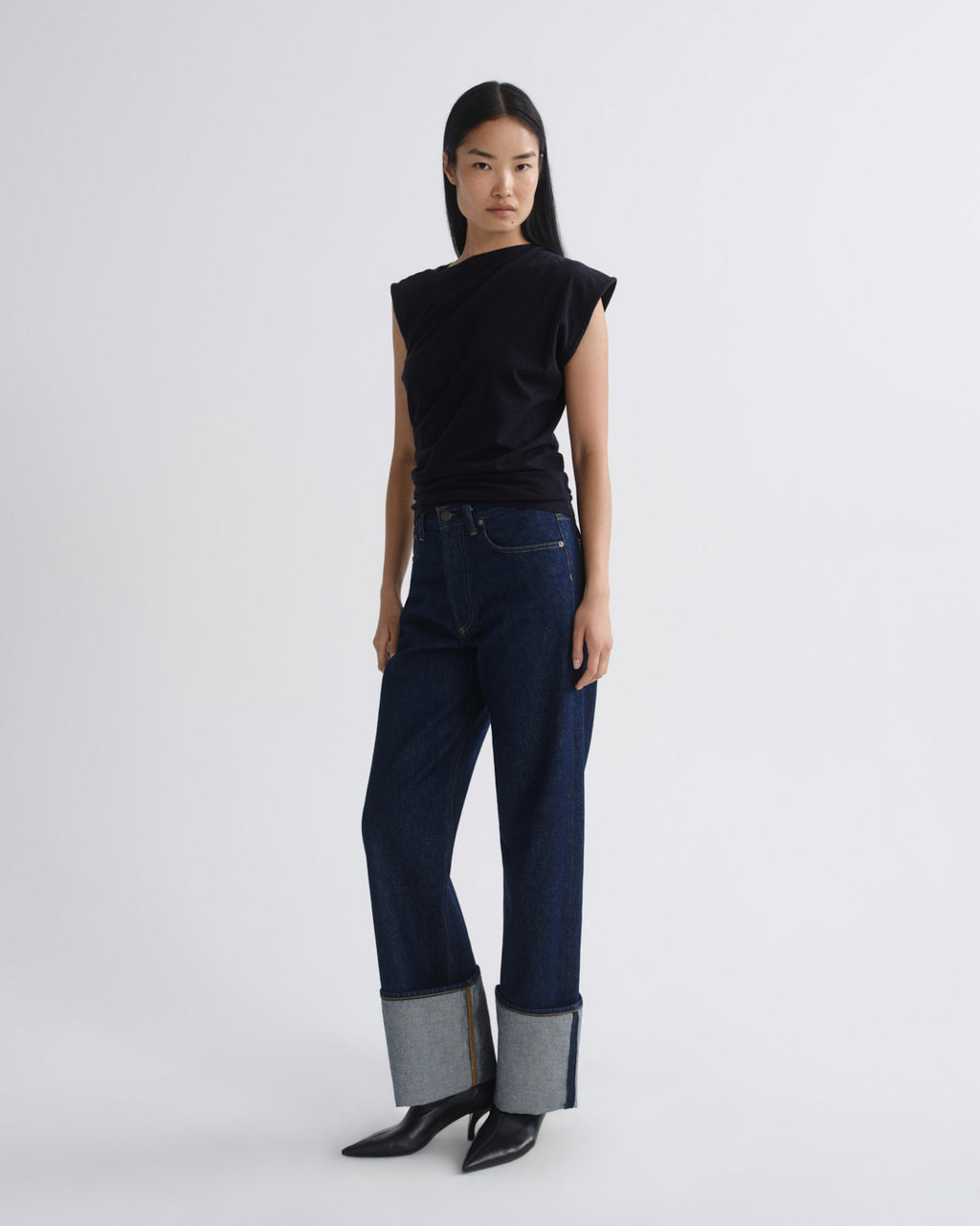 Woman wearing a navy sleeveless top and dark blue jeans on a white background