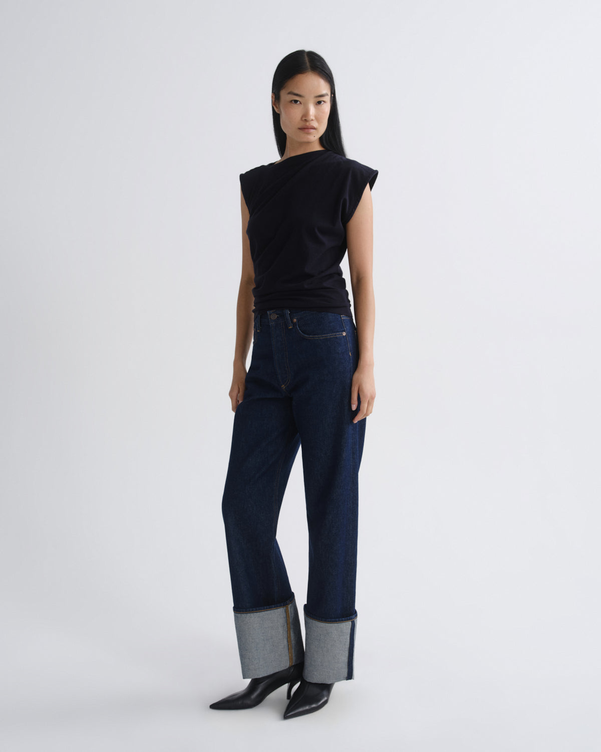 Woman wearing a navy sleeveless top and dark blue jeans on a white background