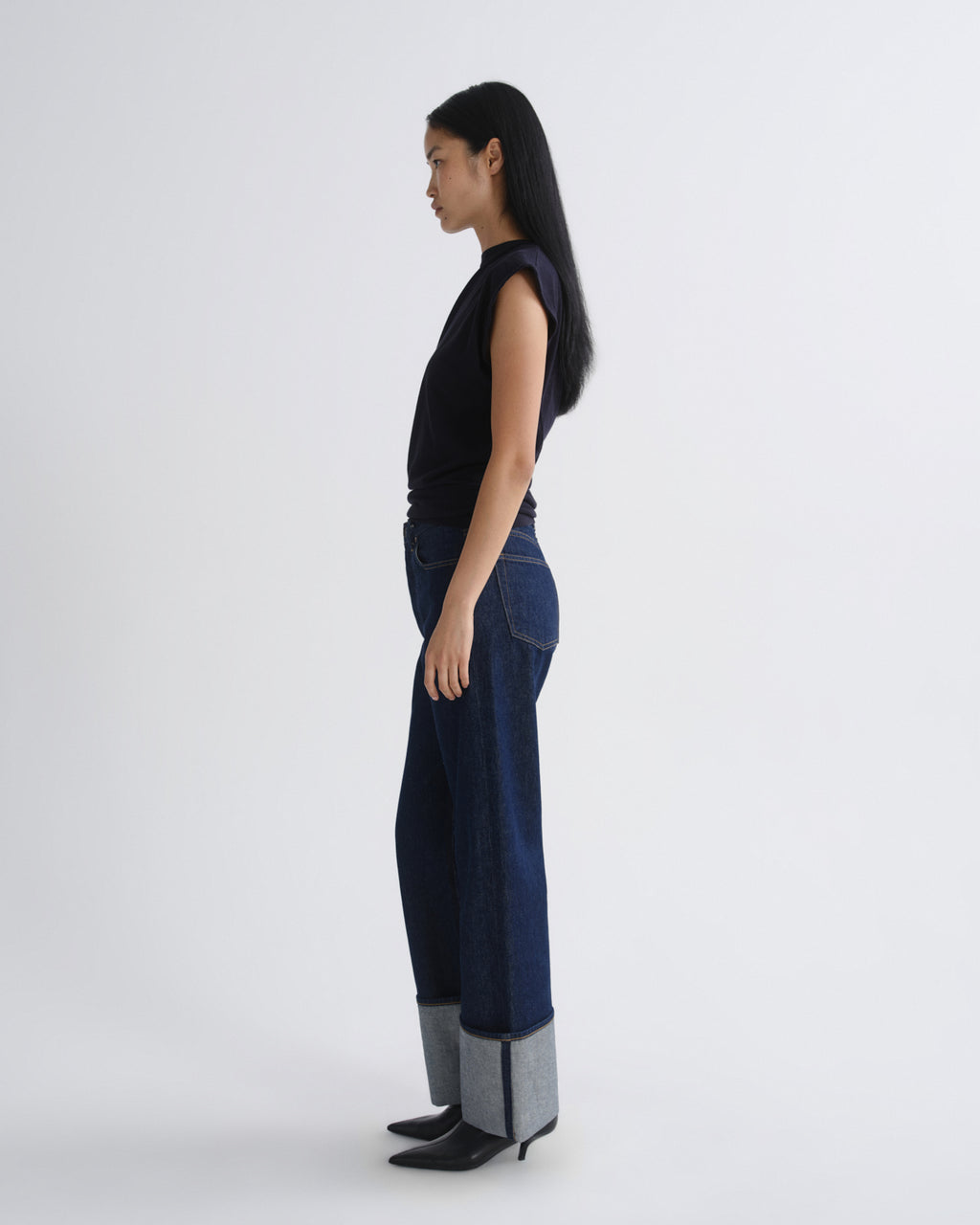 Woman wearing a navy sleeveless top and dark blue jeans on a white background