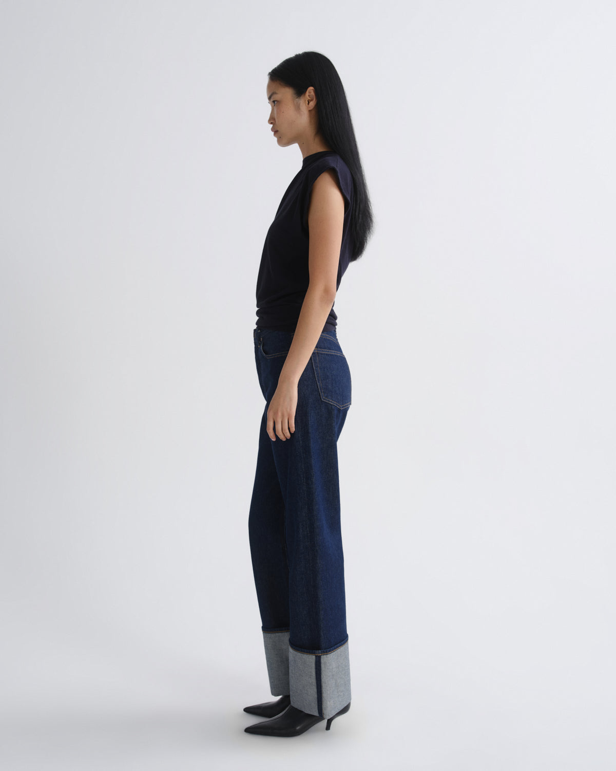 Woman wearing a navy sleeveless top and dark blue jeans on a white background