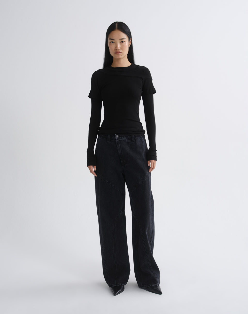 A model stands against a grey background wearing a fitted black long-sleeve top with cap sleeves and black wide-leg pants.