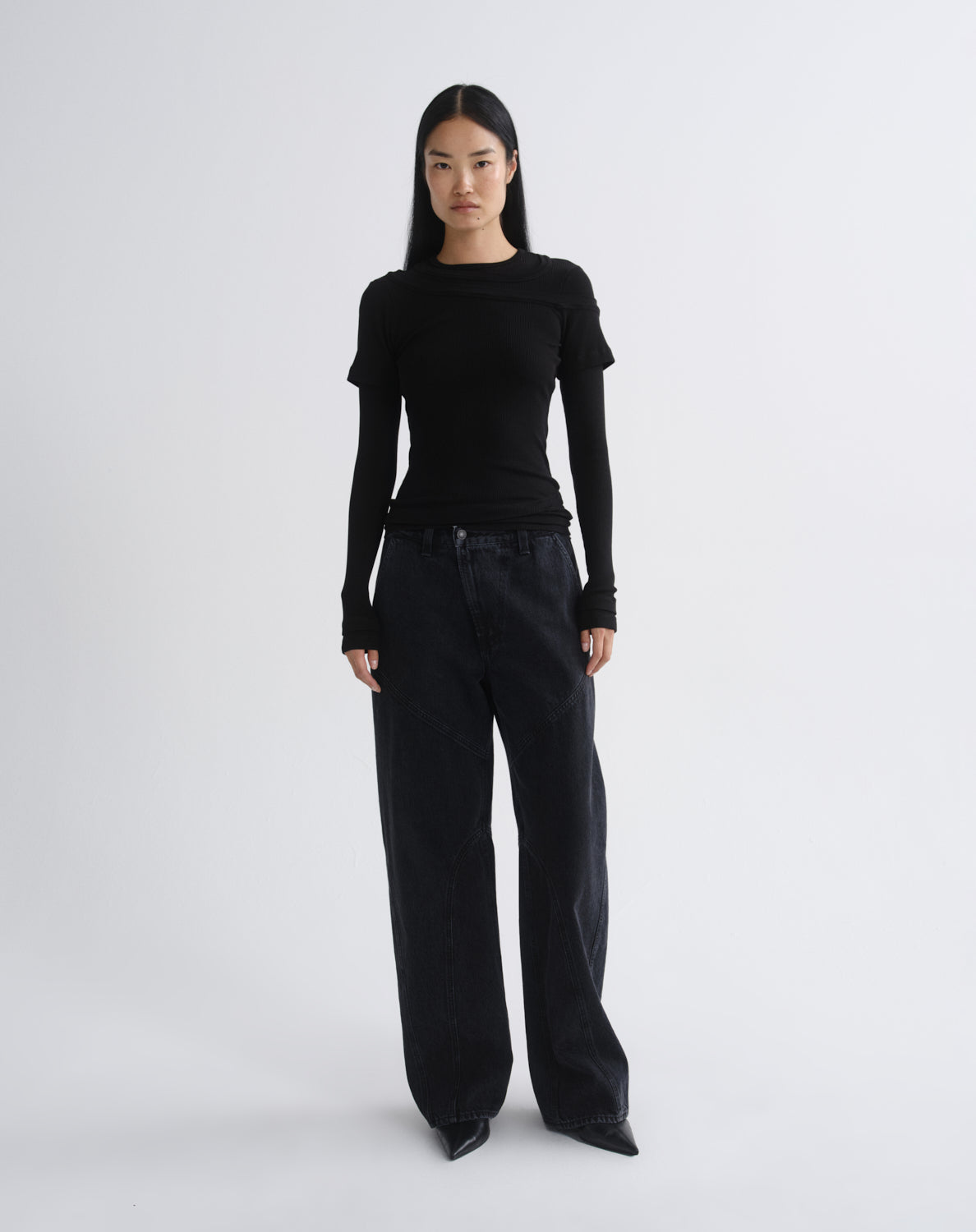 A model stands against a grey background wearing a fitted black long-sleeve top with cap sleeves and black wide-leg pants.
