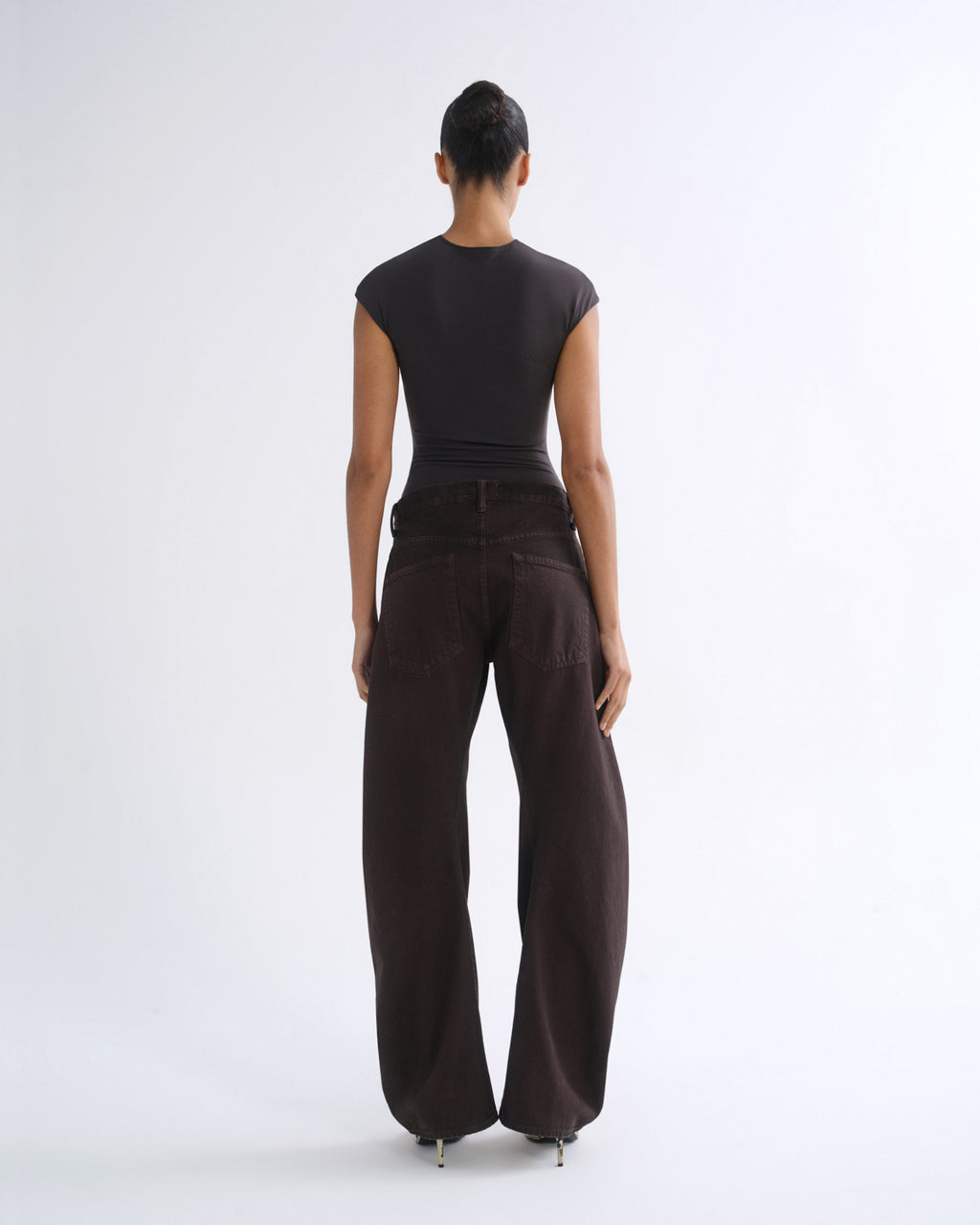 A model shown from the back wearing a black short-sleeve top and dark brown wide-leg pants against a plain white studio background.