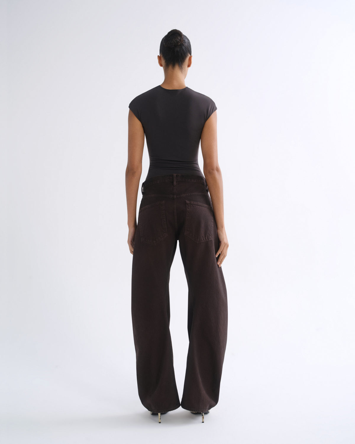 A model shown from the back wearing a black short-sleeve top and dark brown wide-leg pants against a plain white studio background.