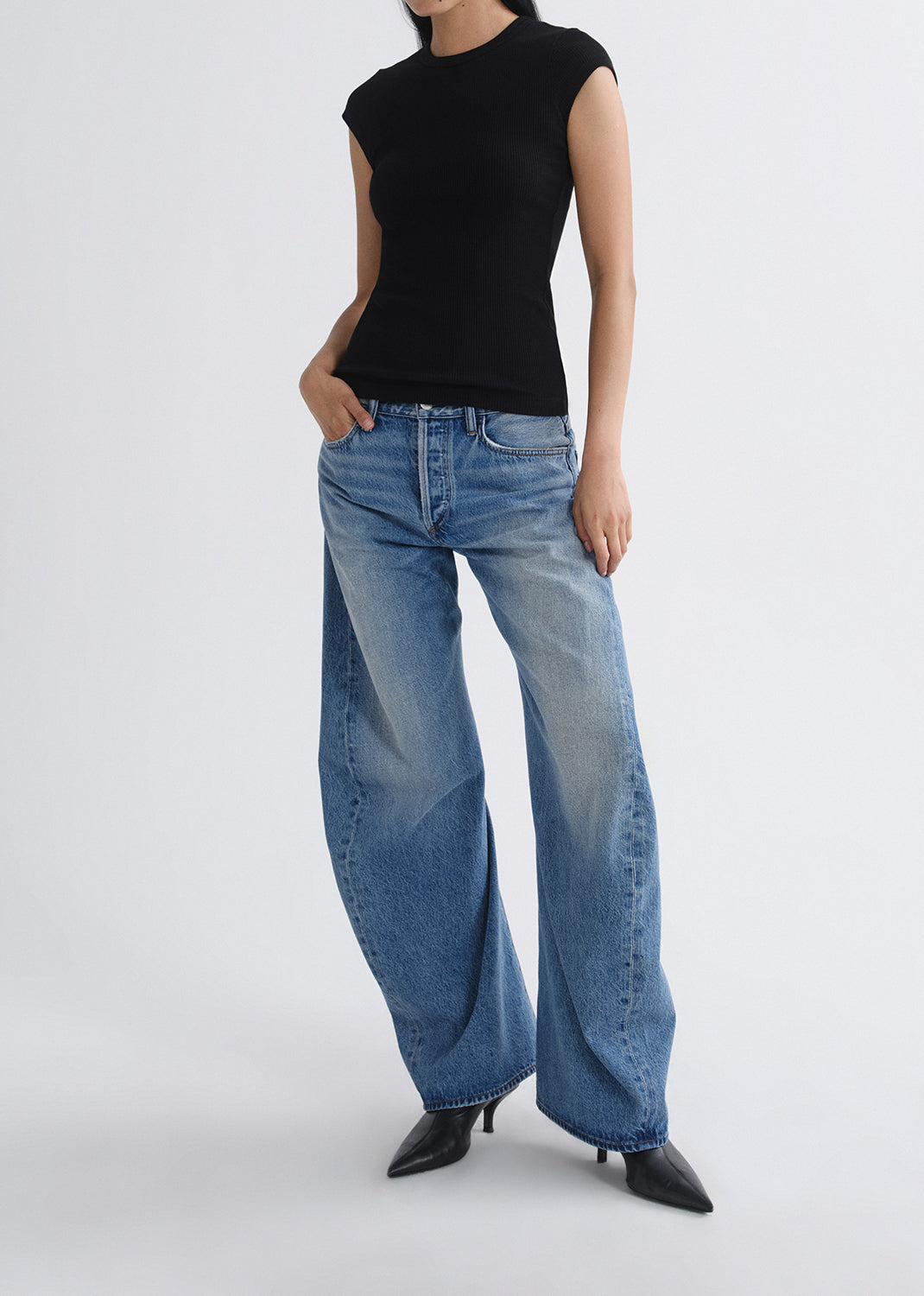 Person wearing a black top and blue jeans on a grey background