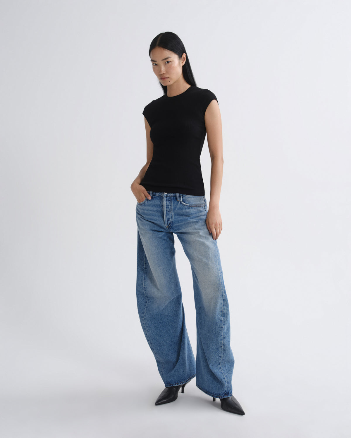 Woman wearing a black sleeveless top and blue jeans on a white background