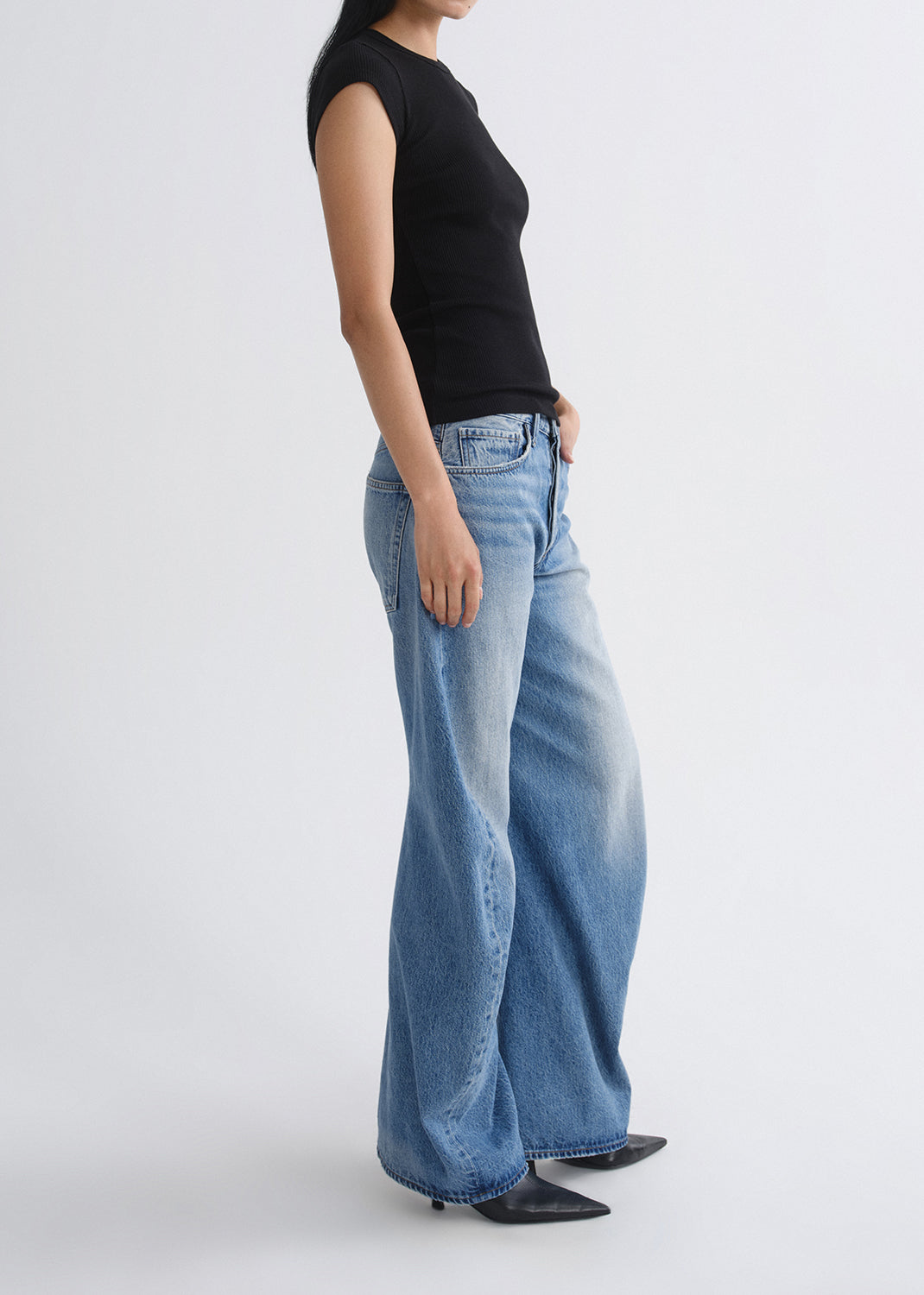 Person wearing a black sleeveless top and light blue jeans on a grey background