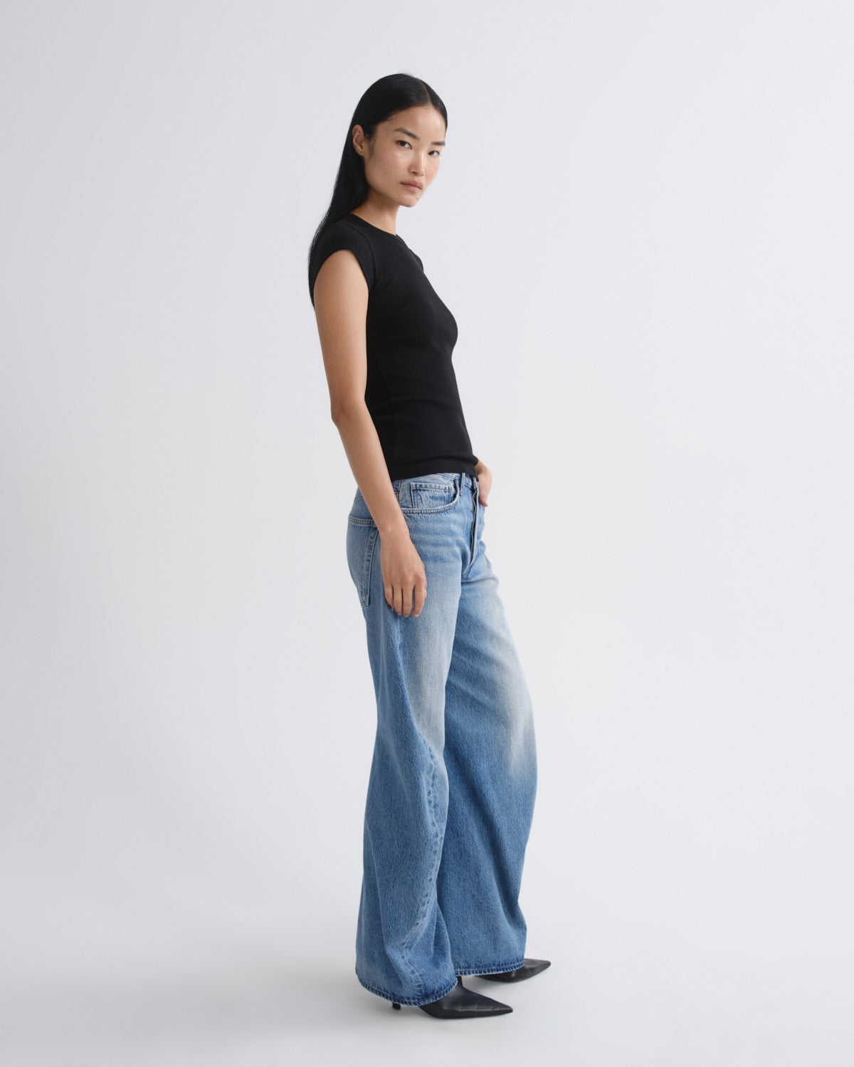 Person wearing a black top and blue jeans on a white background