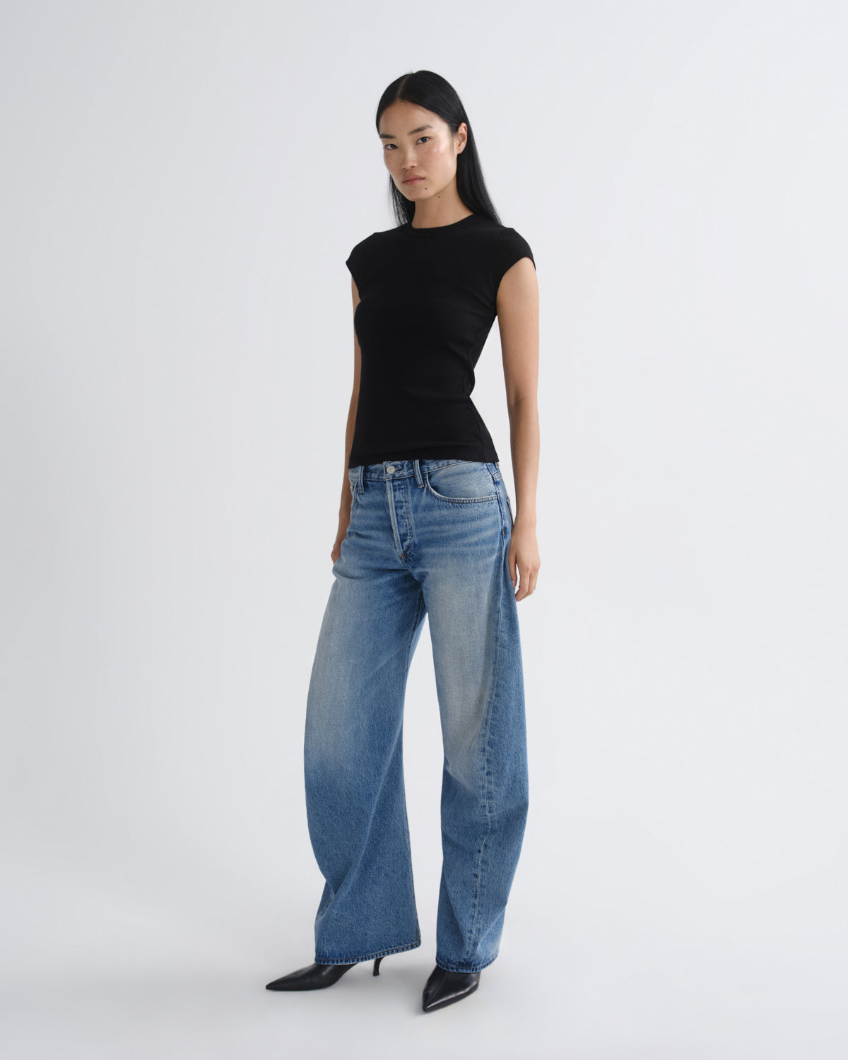 Woman wearing a black top and blue jeans on a white background