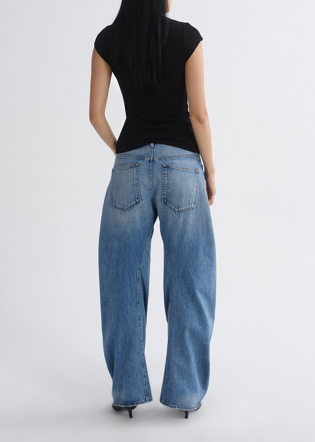 Person wearing blue jeans and a black top on a grey background