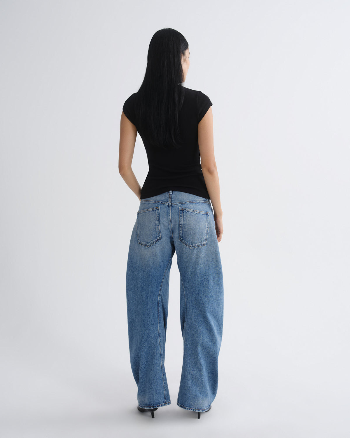 Person wearing blue jeans and a black top on a white background