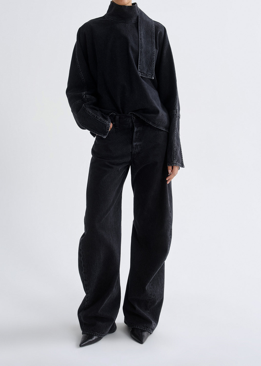 Person wearing a black outfit with wide-leg pants on a grey background