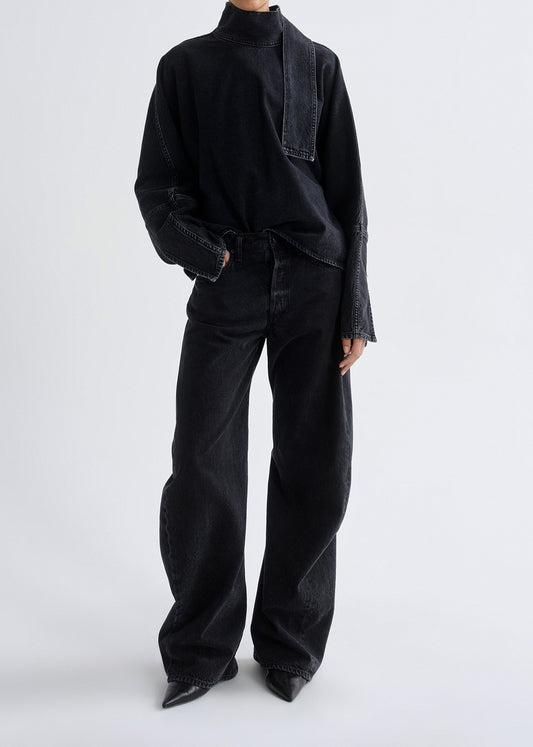Person wearing a black outfit with wide-leg pants on a grey background