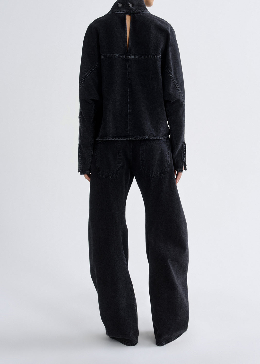 Person wearing a black outfit with wide-leg pants on a grey background