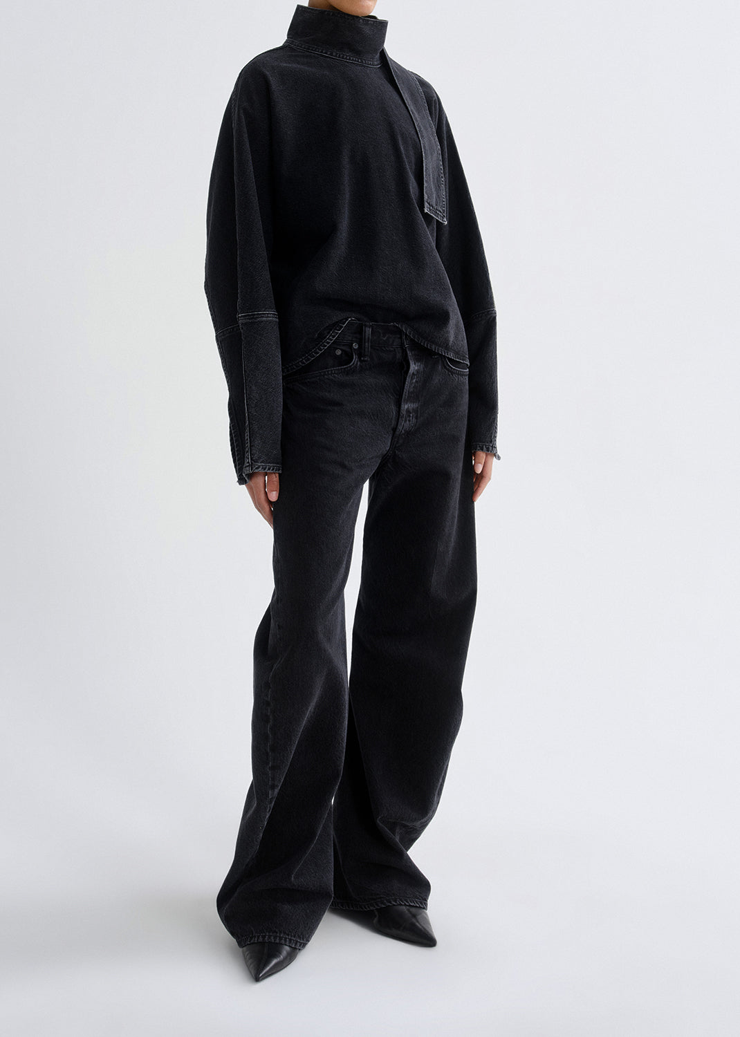 Person wearing a black outfit with wide-leg pants on a grey background
