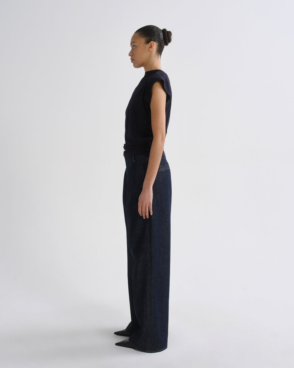 A model in profile wearing a dark navy sleeveless top and matching wide-leg trousers, standing against a plain light gray studio background.