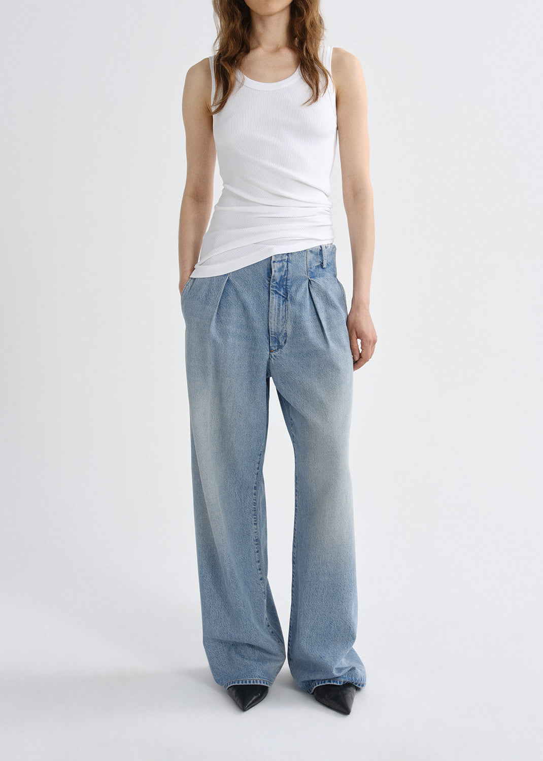 Person wearing a white tank top and light blue jeans on a grey background