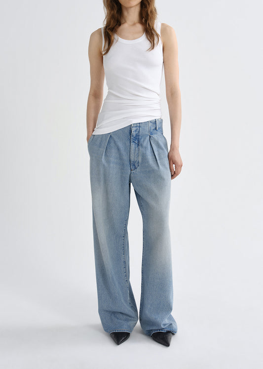 Person wearing a white tank top and light blue jeans on a grey background